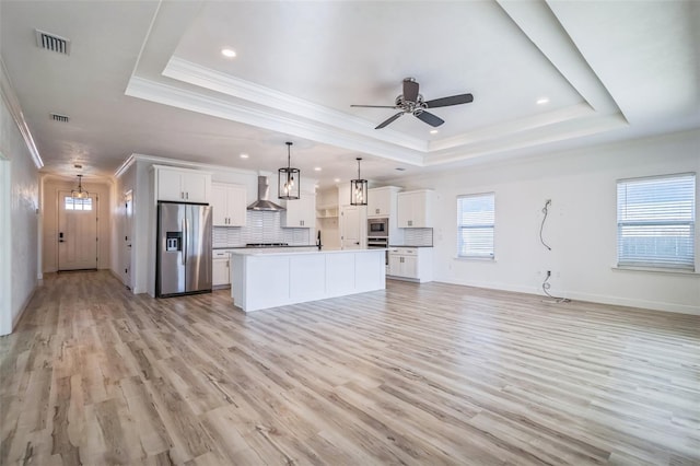 kitchen with stainless steel appliances, wall chimney exhaust hood, a tray ceiling, and white cabinetry