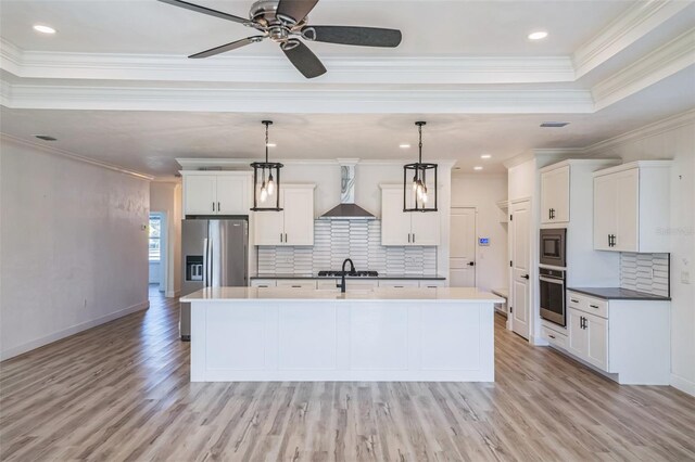 kitchen with a center island with sink, wall chimney range hood, decorative light fixtures, and appliances with stainless steel finishes