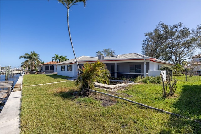 rear view of house featuring a water view, a sunroom, and a lawn