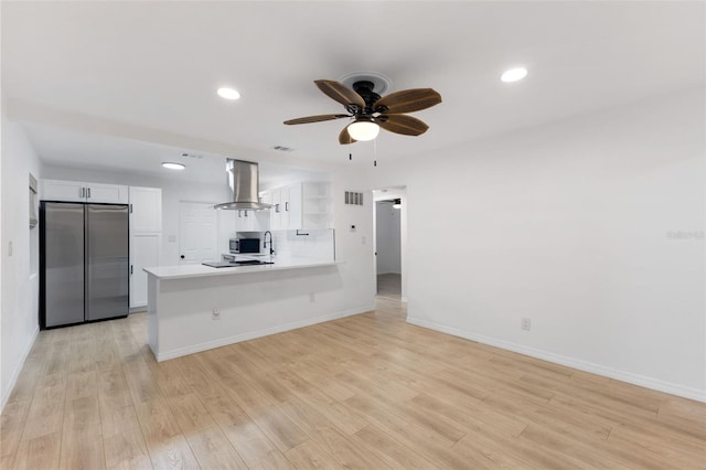 kitchen featuring light hardwood / wood-style floors, kitchen peninsula, island exhaust hood, stainless steel appliances, and white cabinets