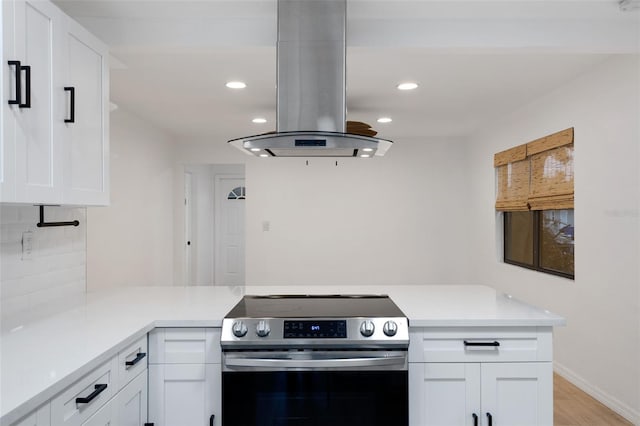 kitchen featuring white cabinets, stainless steel range with electric cooktop, island exhaust hood, backsplash, and kitchen peninsula