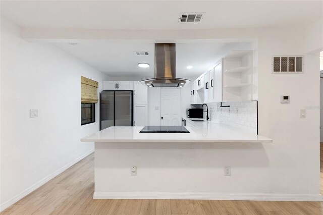 kitchen featuring white cabinetry, sink, kitchen peninsula, island range hood, and stainless steel refrigerator