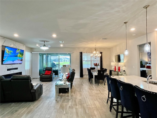 living room with ceiling fan with notable chandelier, light hardwood / wood-style flooring, and sink