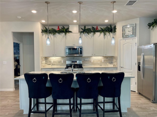 kitchen featuring pendant lighting, an island with sink, white cabinets, and appliances with stainless steel finishes