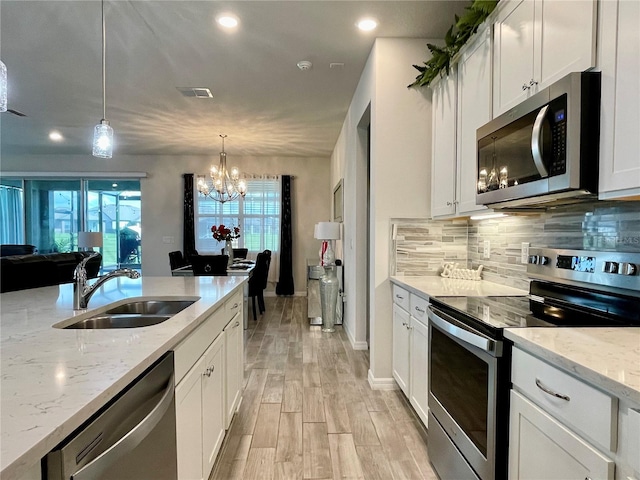 kitchen featuring sink, stainless steel appliances, light stone countertops, hanging light fixtures, and white cabinetry