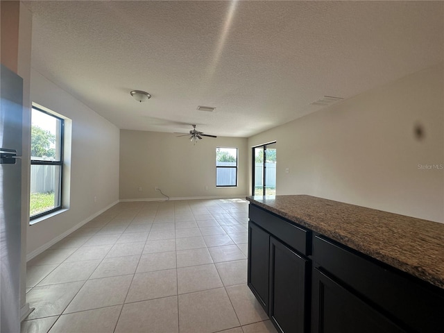 unfurnished living room featuring ceiling fan, light tile patterned floors, and a textured ceiling