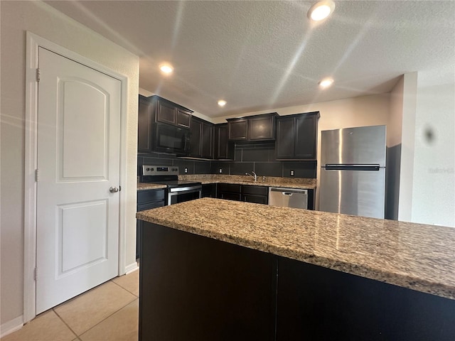 kitchen with light stone countertops, appliances with stainless steel finishes, backsplash, a textured ceiling, and light tile patterned floors