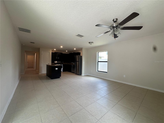 unfurnished living room featuring ceiling fan, light tile patterned floors, and a textured ceiling