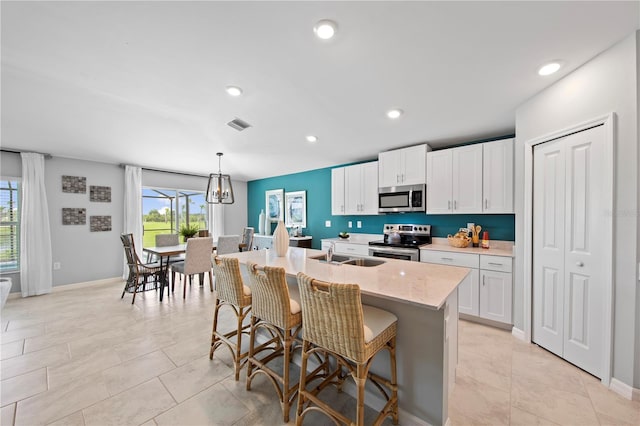 kitchen with white cabinets, a kitchen island with sink, decorative light fixtures, appliances with stainless steel finishes, and a kitchen bar