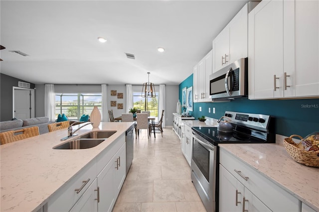 kitchen with light stone countertops, appliances with stainless steel finishes, hanging light fixtures, and white cabinetry