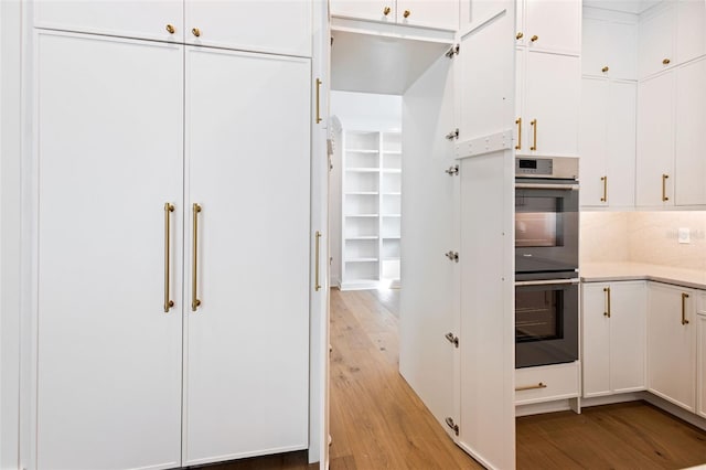 kitchen with stainless steel double oven, white cabinetry, light hardwood / wood-style floors, and tasteful backsplash