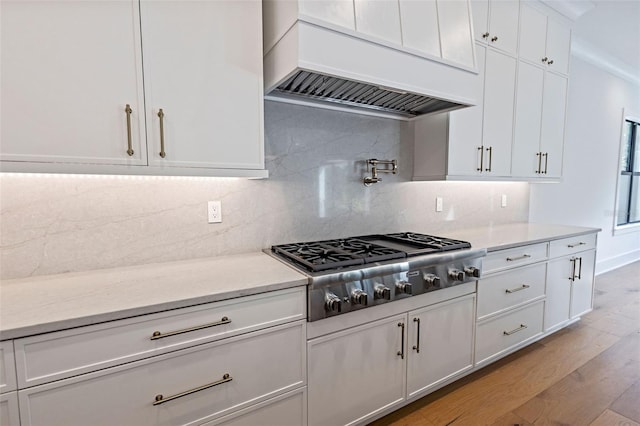 kitchen featuring tasteful backsplash, light hardwood / wood-style flooring, stainless steel gas stovetop, custom exhaust hood, and white cabinetry