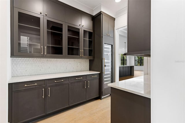 kitchen featuring ornamental molding, light wood-type flooring, dark brown cabinetry, and tasteful backsplash