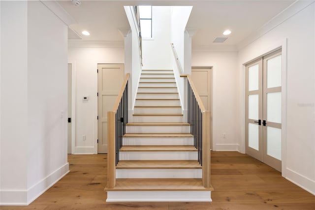 stairs with french doors, crown molding, and hardwood / wood-style floors