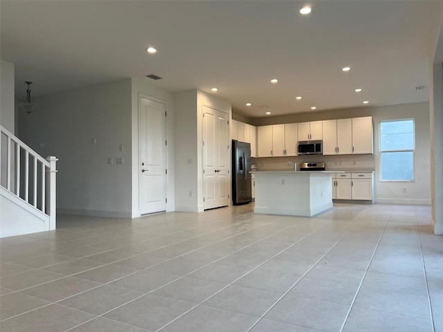 kitchen featuring white cabinets, light tile patterned flooring, stainless steel appliances, and an island with sink