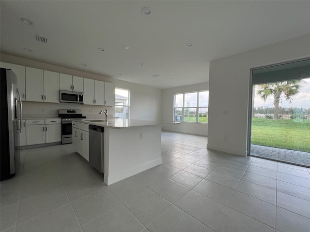 kitchen featuring appliances with stainless steel finishes, sink, light tile patterned floors, a center island with sink, and white cabinets