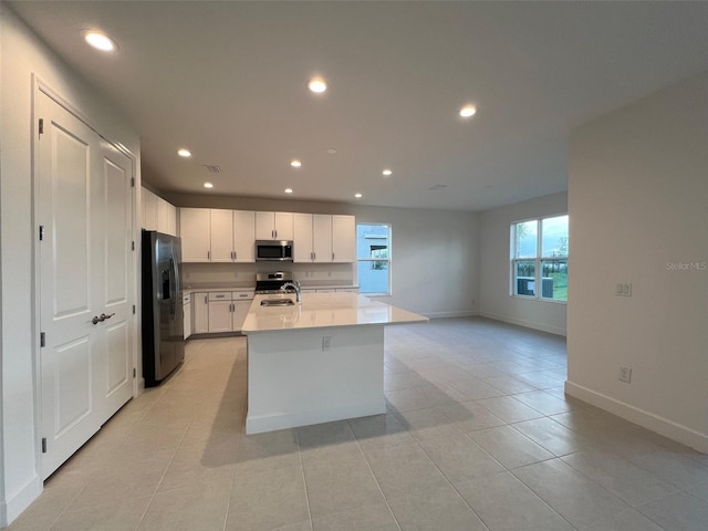 kitchen with appliances with stainless steel finishes, sink, light tile patterned floors, a center island with sink, and white cabinetry