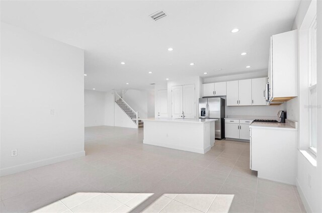 kitchen featuring sink, light tile patterned flooring, a kitchen island, stainless steel fridge, and white cabinets