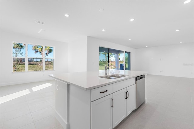 kitchen with an island with sink, white cabinets, stainless steel dishwasher, light tile patterned floors, and sink