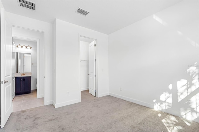 unfurnished bedroom with light colored carpet, sink, a closet, a spacious closet, and ensuite bathroom