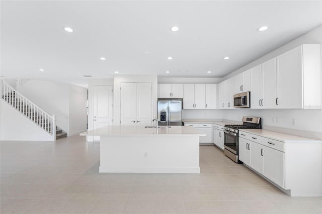 kitchen with a center island with sink, light tile patterned floors, sink, white cabinetry, and stainless steel appliances