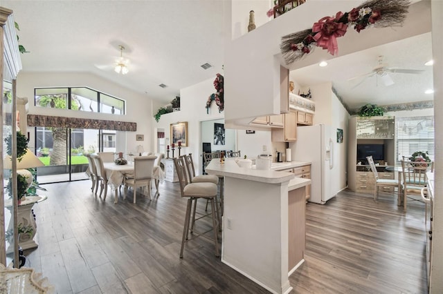 kitchen featuring ceiling fan, dark hardwood / wood-style flooring, a kitchen bar, vaulted ceiling, and white refrigerator with ice dispenser