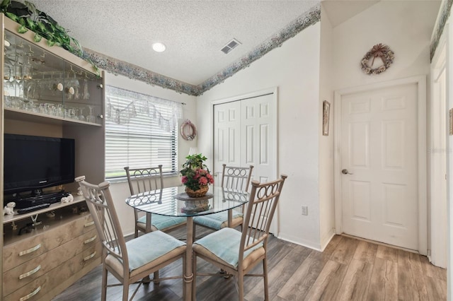 dining area featuring lofted ceiling, a textured ceiling, and hardwood / wood-style flooring