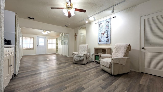 living area featuring dark wood-type flooring, visible vents, a textured ceiling, and a ceiling fan