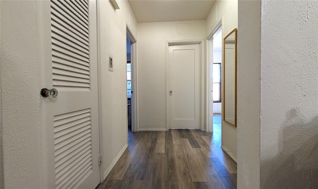 hall featuring dark wood-style floors, baseboards, and a textured wall