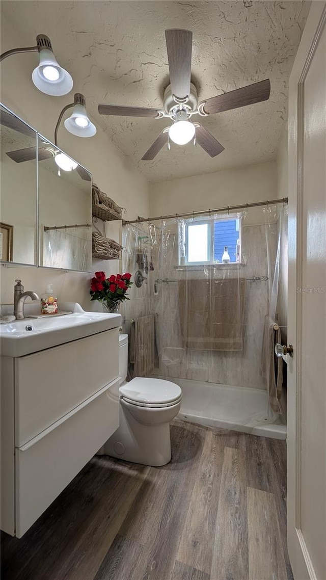 full bath featuring a textured ceiling, ceiling fan, toilet, wood finished floors, and vanity