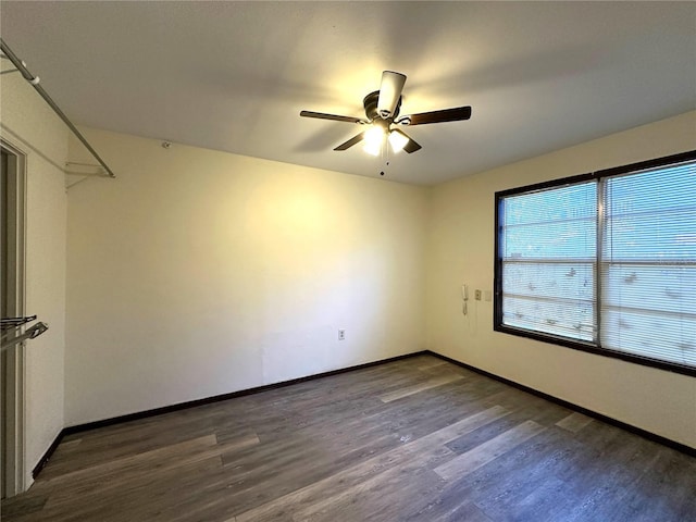 empty room with dark wood finished floors, baseboards, and ceiling fan