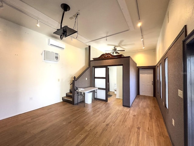 interior space featuring light wood-style flooring, ceiling fan, stairway, rail lighting, and an AC wall unit