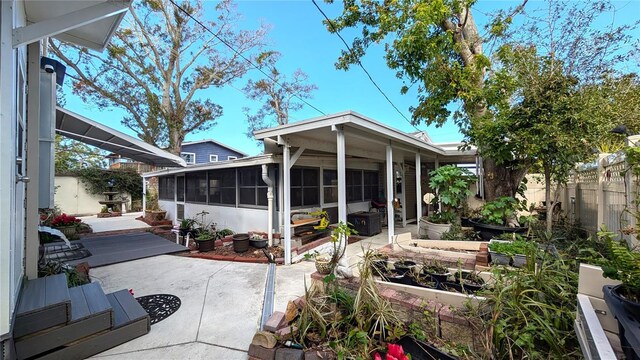 rear view of property with a vegetable garden, a sunroom, fence, and a patio