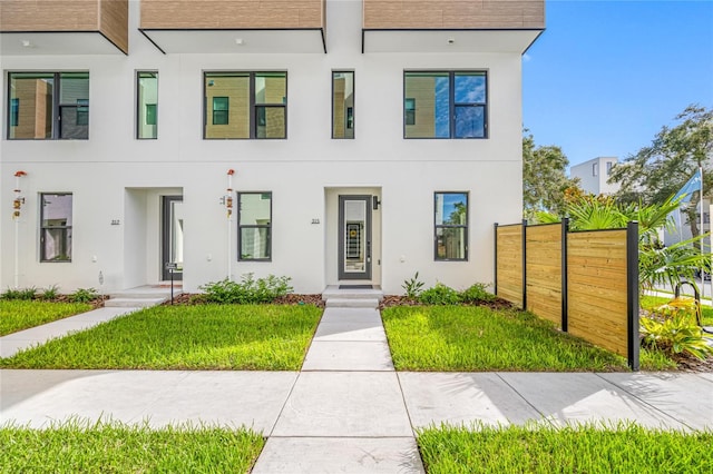 townhome / multi-family property with a front yard, fence, and stucco siding