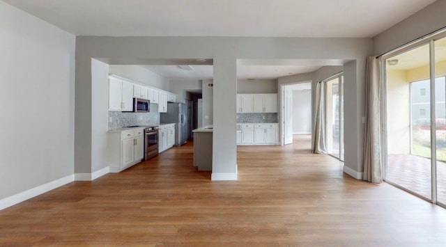 kitchen with decorative backsplash, light hardwood / wood-style floors, white cabinets, and appliances with stainless steel finishes