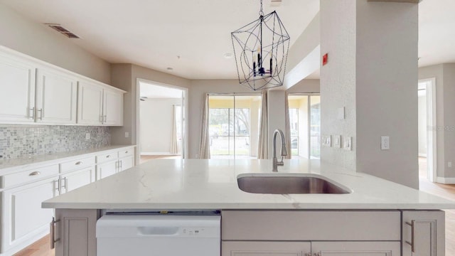 kitchen with sink, a notable chandelier, light stone counters, and white cabinetry