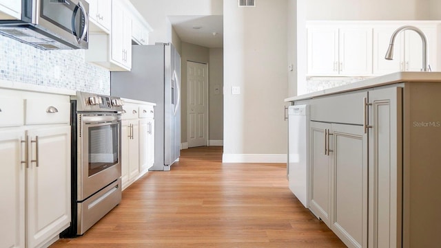 kitchen featuring stainless steel appliances, backsplash, light hardwood / wood-style flooring, and white cabinetry