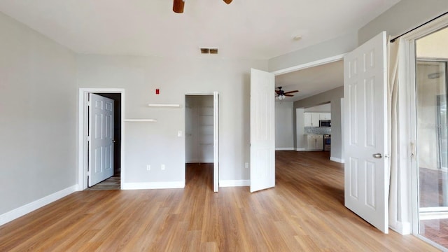 unfurnished bedroom featuring ceiling fan, a closet, light hardwood / wood-style floors, and a walk in closet