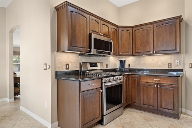 kitchen with decorative backsplash, dark stone counters, appliances with stainless steel finishes, and light tile patterned floors