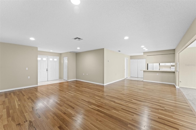 unfurnished living room with light hardwood / wood-style flooring and a textured ceiling