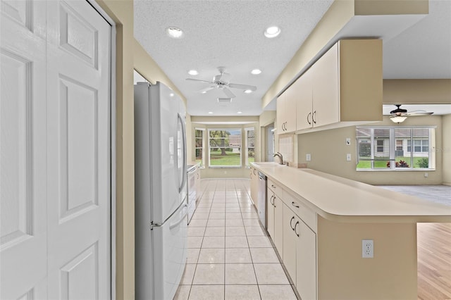 kitchen with kitchen peninsula, a textured ceiling, light tile patterned floors, and white appliances