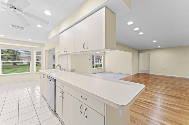 kitchen with sink, dishwasher, kitchen peninsula, light hardwood / wood-style floors, and white cabinets