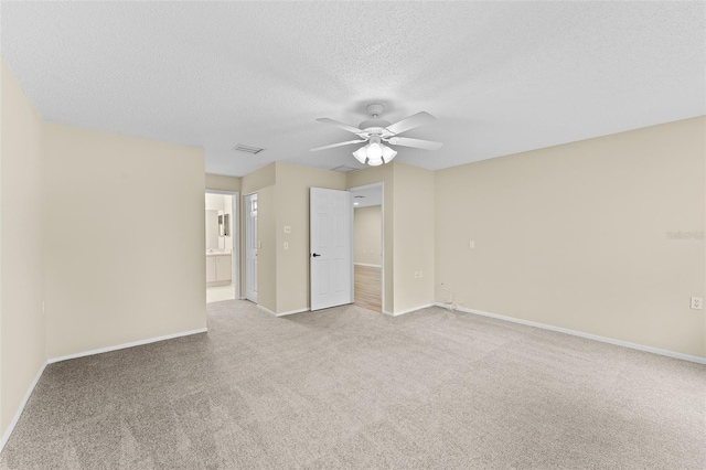 spare room with a textured ceiling, light colored carpet, and ceiling fan