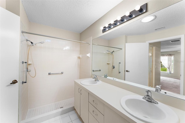 bathroom with vanity, tiled shower, a textured ceiling, and tile patterned flooring