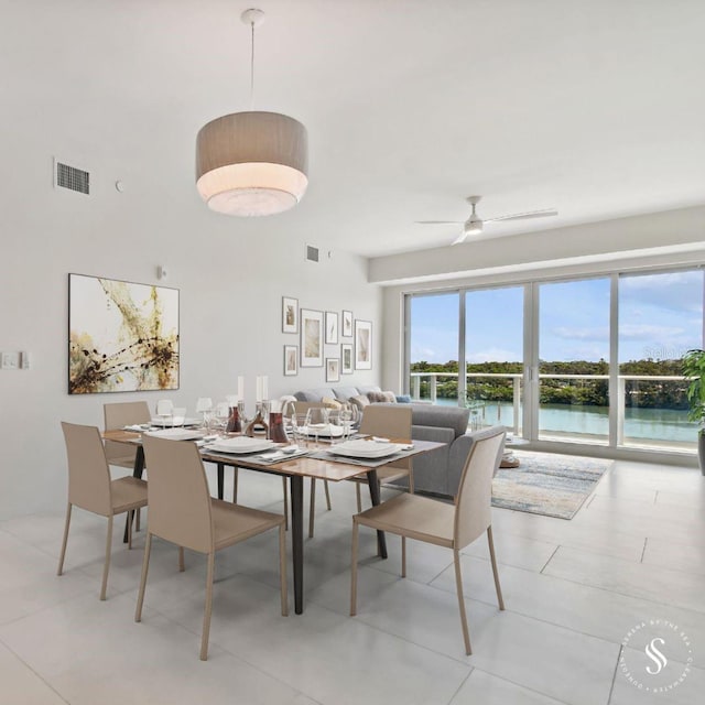 dining room featuring light tile patterned flooring, a water view, and ceiling fan