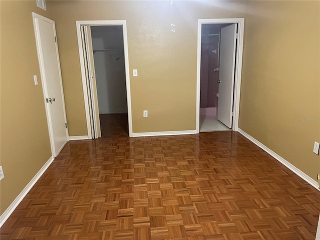 unfurnished bedroom with a spacious closet, ensuite bathroom, a closet, and dark parquet floors