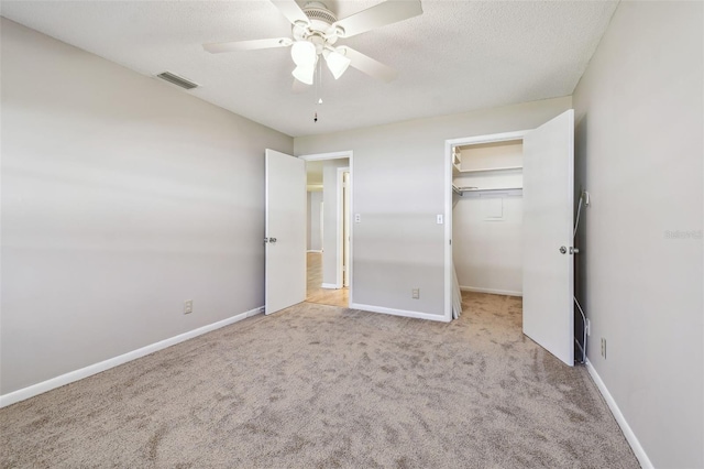 unfurnished bedroom with light carpet, a walk in closet, a textured ceiling, ceiling fan, and a closet