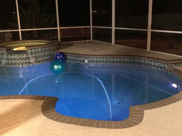 pool at twilight featuring an in ground hot tub and glass enclosure