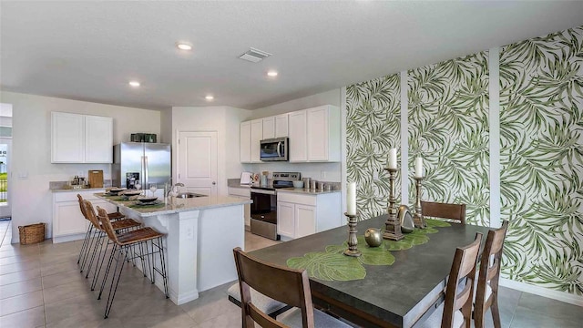 kitchen featuring light stone counters, white cabinets, appliances with stainless steel finishes, a kitchen bar, and a center island with sink