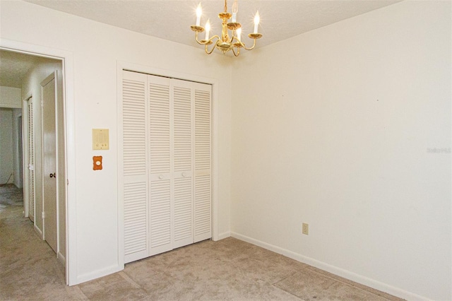 unfurnished bedroom with a textured ceiling, a closet, an inviting chandelier, and light colored carpet